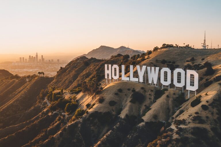Hollywood sign perched on hillside with LA skyline visible in distance at sunset.