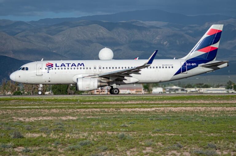 White LATAM Airbus A320 on a runway with a mountainous backdrop, landing gear down, airline logo visible on fuselage and tail.