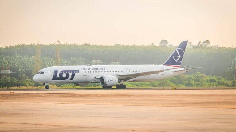 LOT Polish Airlines airplane on a taxiway with a green treeline in the background, side view of the aircraft tail logo visible
