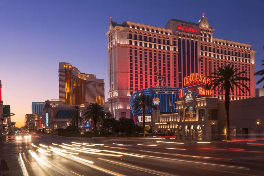 Las Vegas Strip at dusk with neon hotel signs, tall buildings, and light trails from passing cars.