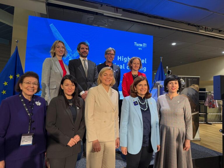 Ten professionals pose for a group photo on a stage with a blue backdrop and European Union flag on the left.