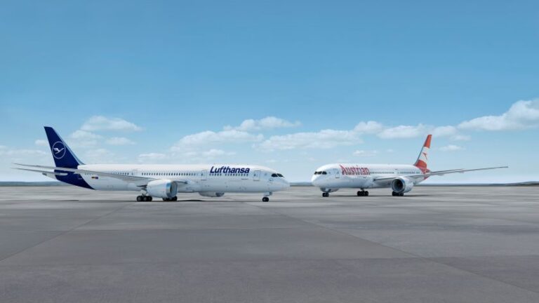 Two commercial airliners, Lufthansa and Austrian Airlines, parked side by side on an airport tarmac under a clear blue sky.