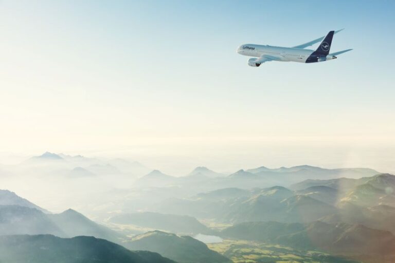 Lufthansa passenger plane flying above a misty mountain range at sunrise.