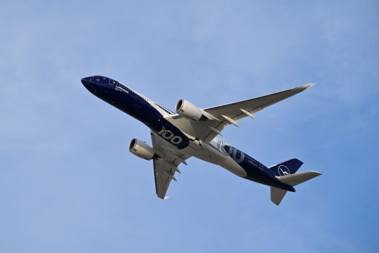 Lufthansa passenger jet in blue livery flying through a clear blue sky, seen from below.