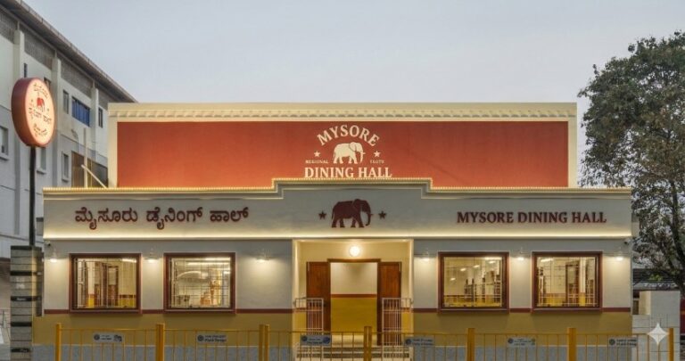 Facade of Mysore Dining Hall: a two-story beige-and-cream building with a red sign and elephant logo above the entrance, Kannada and English text on the front.