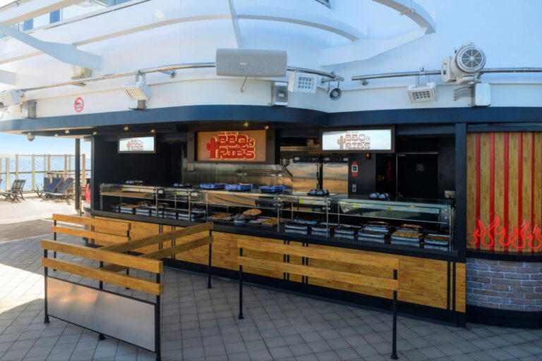 Outdoor barbecue and fries counter on a cruise ship deck, with food trays behind glass and the ocean in the background.