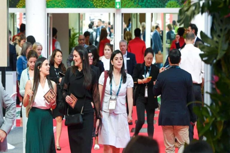 Group of professionals with badges walking through a crowded conference hall on a red carpet.