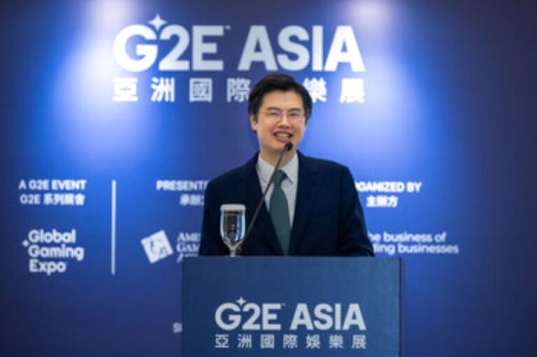 Man in a suit giving a speech at the G2E Asia conference podium on a blue backdrop.