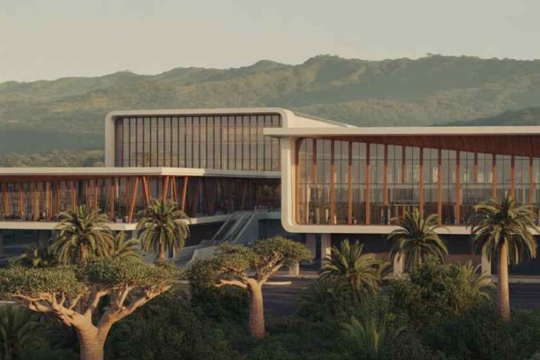 Modern glass-fronted building with curved white frames, surrounded by palm trees and desert hills in the distance.