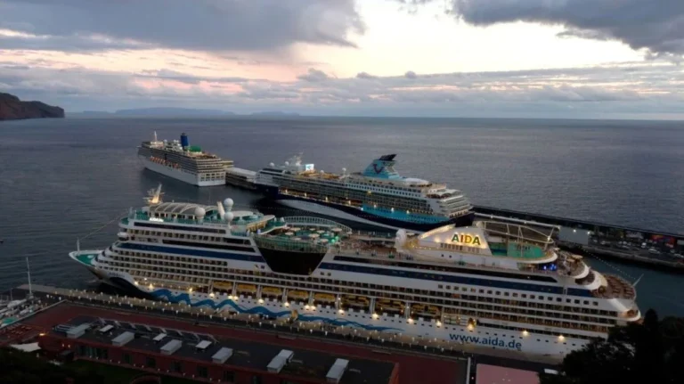 AIDA cruise ship moored at a harbor with other ships nearby and a calm sea at dusk.