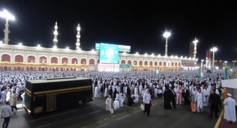 Nighttime view of thousands of pilgrims in white ihram garments gathered in front of a long colonnade with minarets nearby.