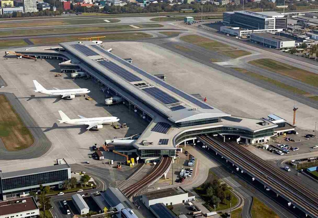 Aerial view of a large airport terminal with several planes docked at gates and rail tracks beside the concourse?