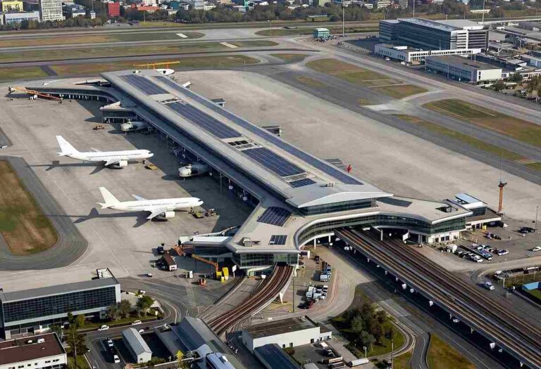Aerial view of a large airport terminal with several planes docked at gates and rail tracks beside the concourse?