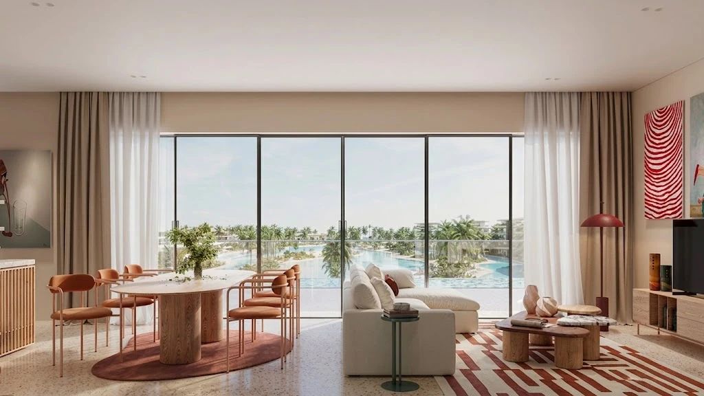 Open-plan living and dining area with a round marble dining table and orange chairs, and a view of a resort pool through floor-to-ceiling glass doors.