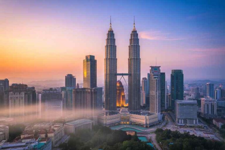 Kuala Lumpur skyline with the Petronas Twin Towers at sunset, connected by a sky bridge among surrounding high-rise buildings.