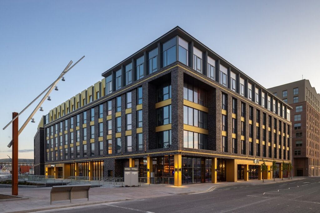 Modern brick office building with large windows and yellow accents along a city street.