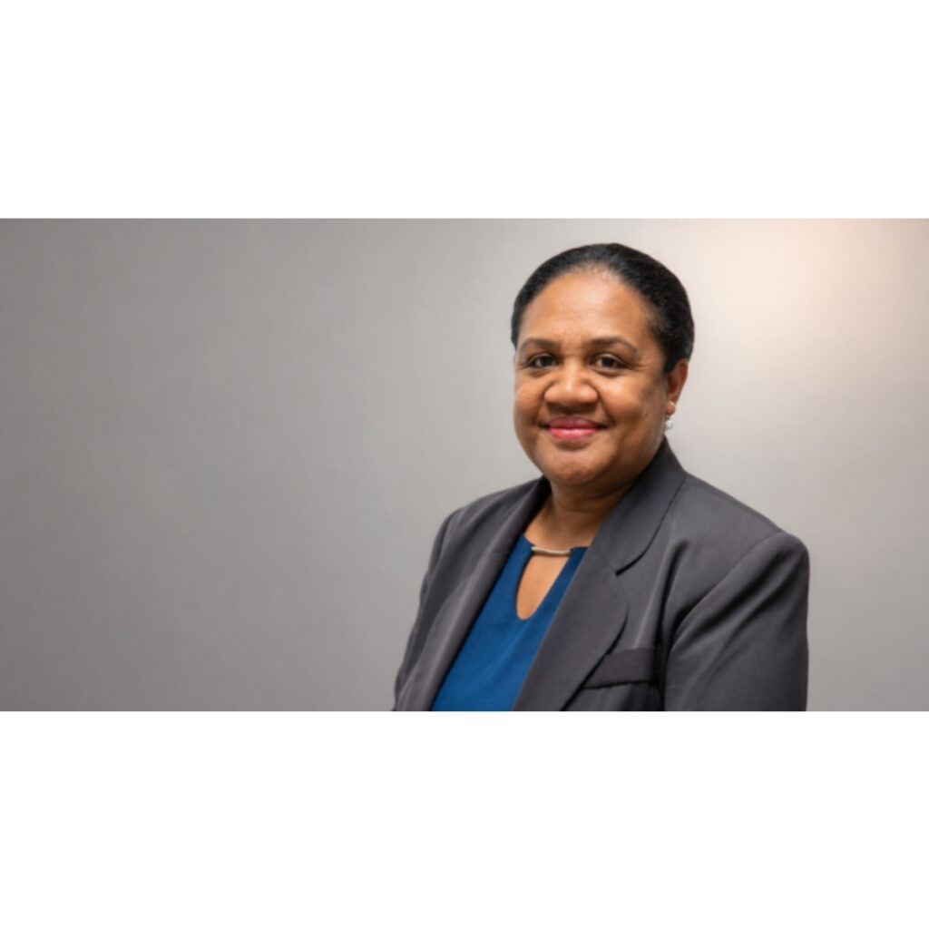 Smiling professional woman in a gray blazer and blue blouse against a neutral backdrop.