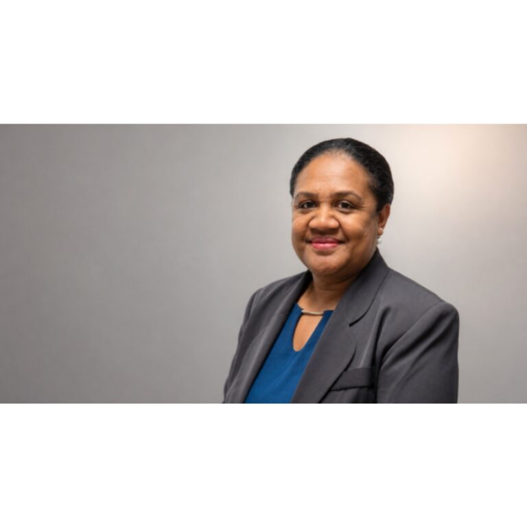 Smiling professional woman in a gray blazer and blue blouse against a neutral backdrop.