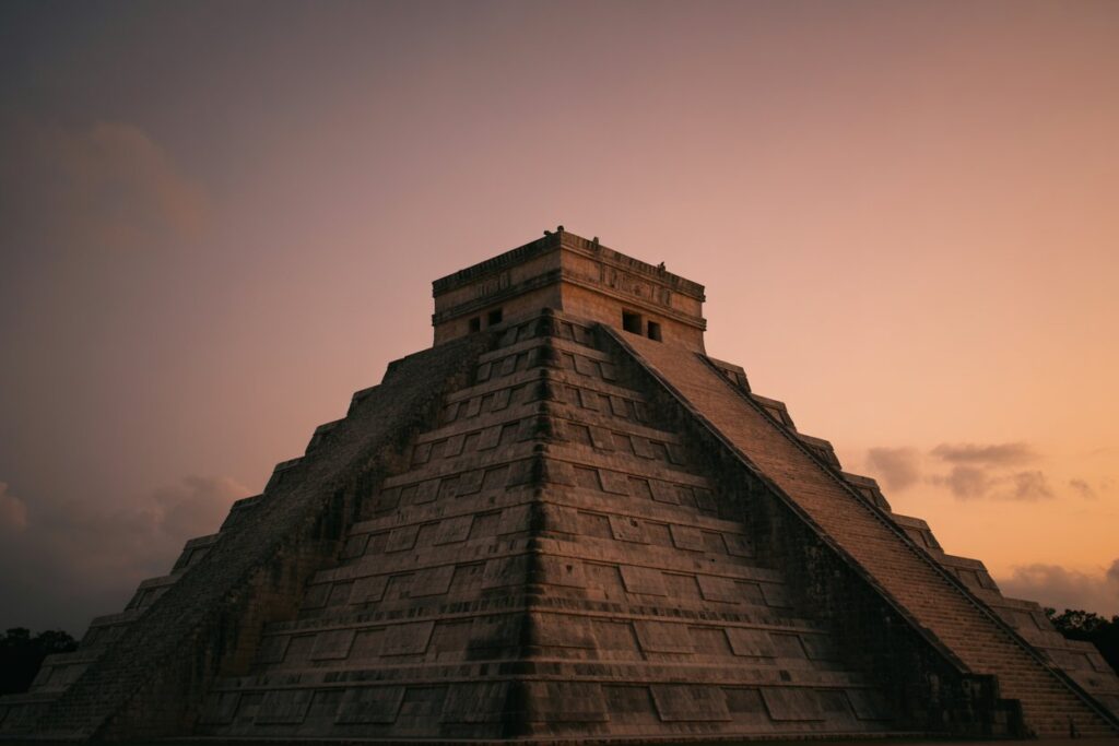 Mayan pyramid with wide stepped terraces at sunset, central staircase on the right side of the structure.