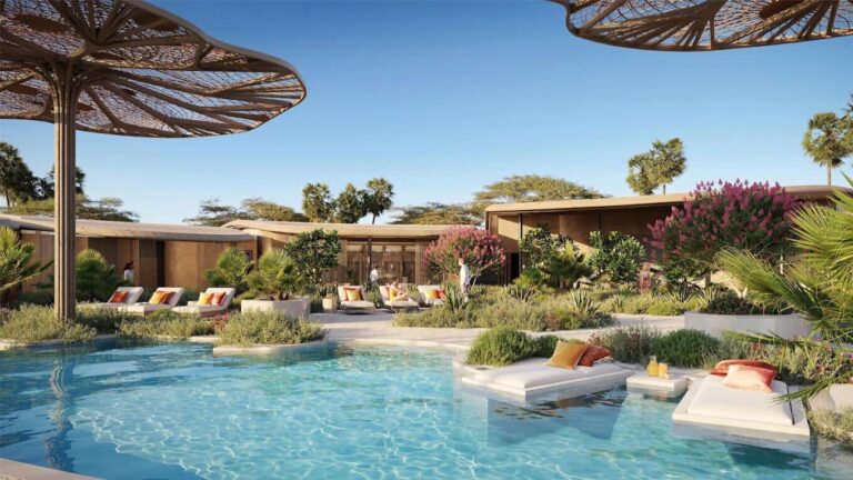 Resort pool with turquoise water, white lounge chairs with orange cushions, and lush tropical plants.