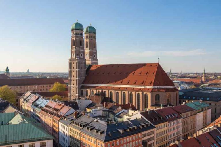 Aerial view of Munich’s Frauenkirche cathedral with two green-domed towers and surrounding colorful rooftops.