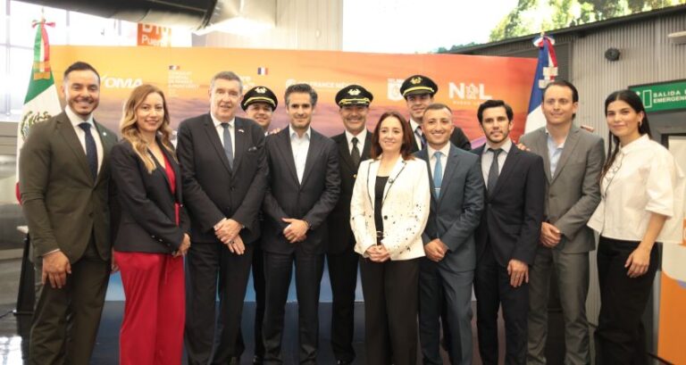 Twelve professionals in suits, with two in captain hats, pose for a photo at a formal event in front of an orange banner with logos.