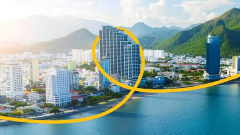 Coastal city skyline with tall buildings along a blue bay, mountains in the background, with a yellow looping graphic overlay.