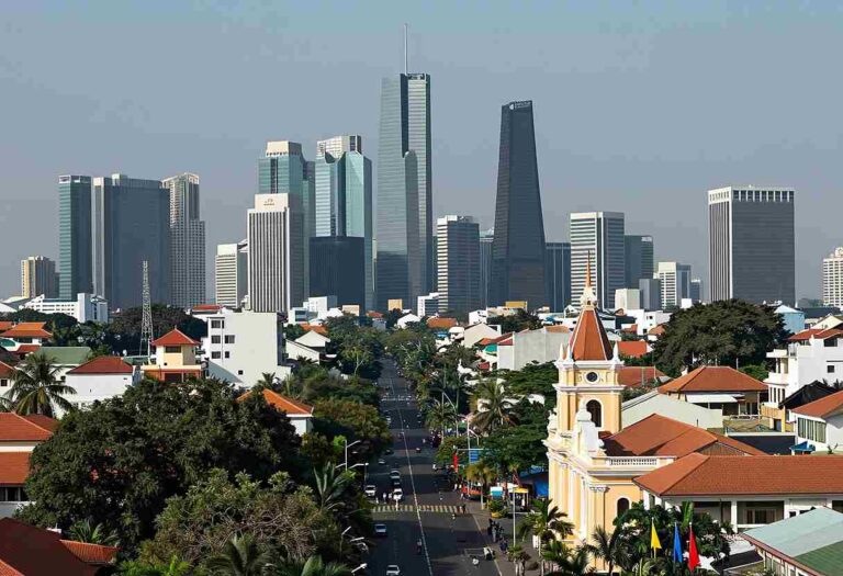 Aerial view of a downtown skyline with tall glass skyscrapers behind a neighborhood of red-tiled houses and a church with a clock tower in the foreground.