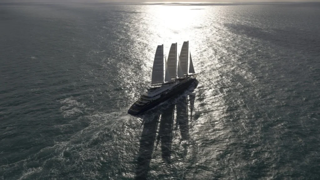 A large four-masted luxury sailing yacht gliding on the sea, sunlight reflecting off the water behind it.