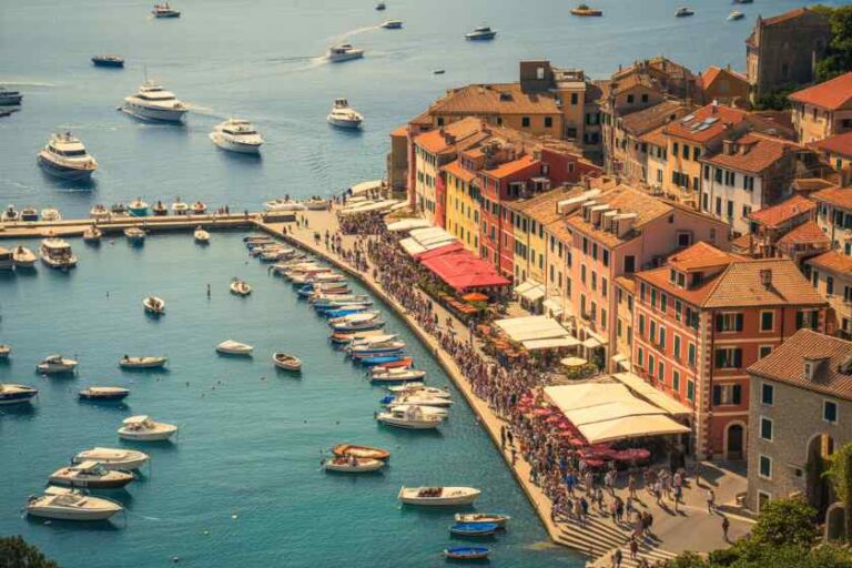 Colorful coastal town with a crowded waterfront promenade beside a busy marina full of boats in calm blue water.