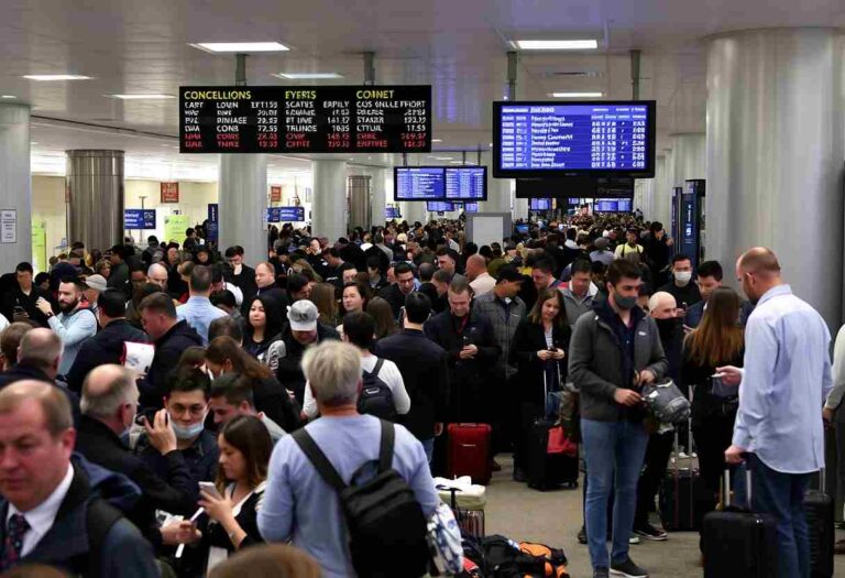 Crowded airport terminal with travelers, luggage, and staff beneath digital departure boards.