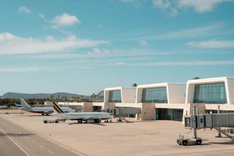 Airport tarmac with a parked passenger plane at a modern terminal gate under a blue sky