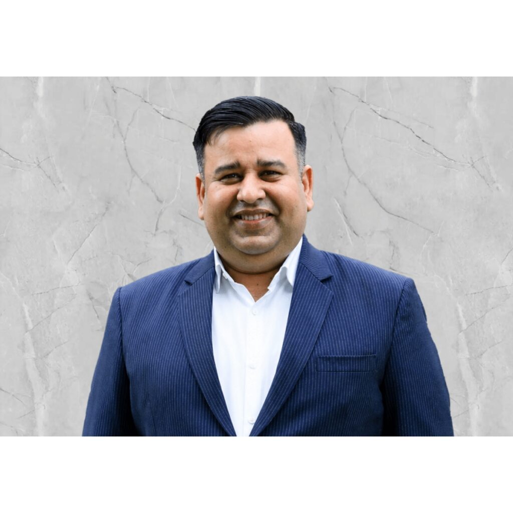 Portrait of a smiling man in a blue pinstripe suit against a gray marble wall.