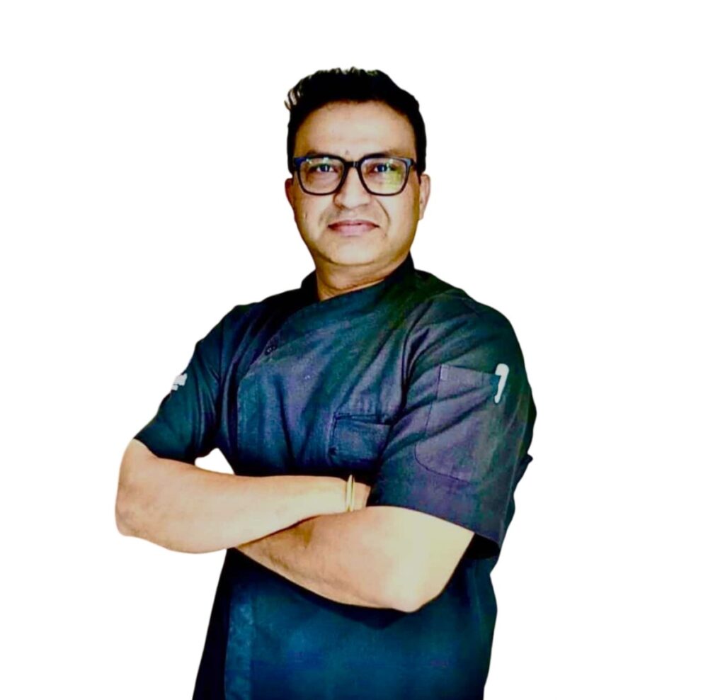 Man wearing dark scrubs with arms crossed, smiling at the camera.