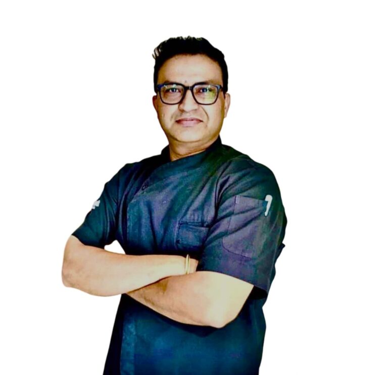 Man wearing dark scrubs with arms crossed, smiling at the camera.
