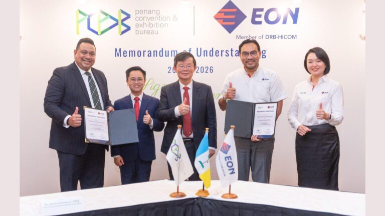 Five professionals standing and smiling, each giving thumbs up after signing a Memorandum of Understanding with EON at a formal event; flags on the table in front.