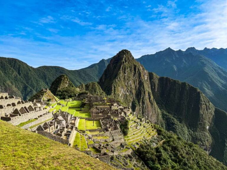 Machu Picchu ruins with stone terraces and temples amid green hills under a bright blue sky.