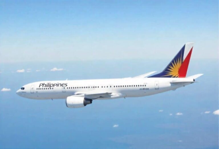White commercial jet with Philippines branding flying high in a clear blue sky, tail featuring Philippine flag design.