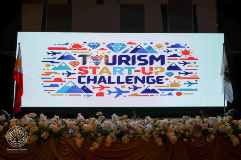 Large LED screen on stage shows 'Tourism Start-Up Challenge' in colorful text with travel icons; Philippine Department of Tourism seal visible bottom left.