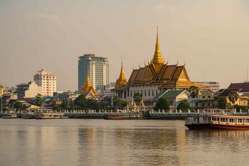 Golden-templed complex along the river with gold-topped roofs and ornate spires, boats on the water nearby.
