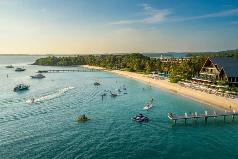 A tropical beach resort with palm trees, a sandy shore, and people enjoying water activities near a wooden pier.