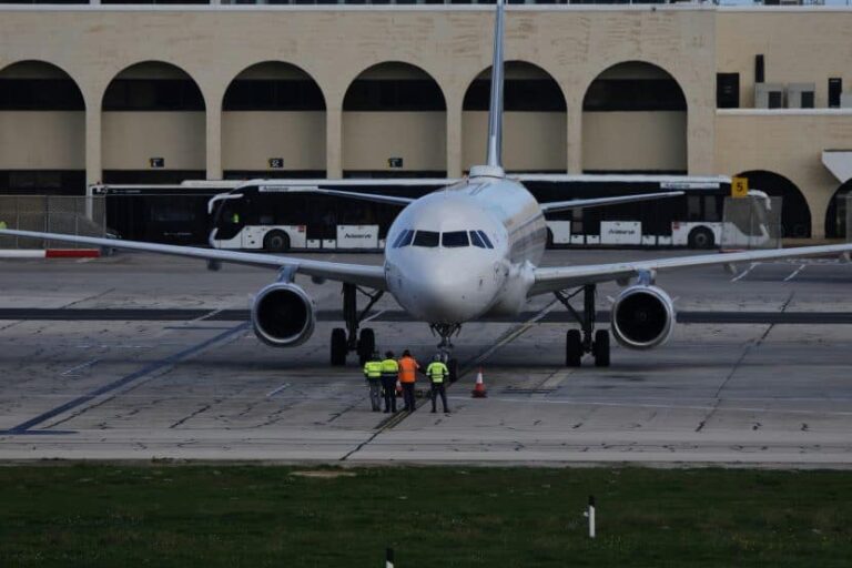 Commercial airplane on the taxiway with ground crew inspecting the nose gear area in high-visibility vests near the aircraft's front.