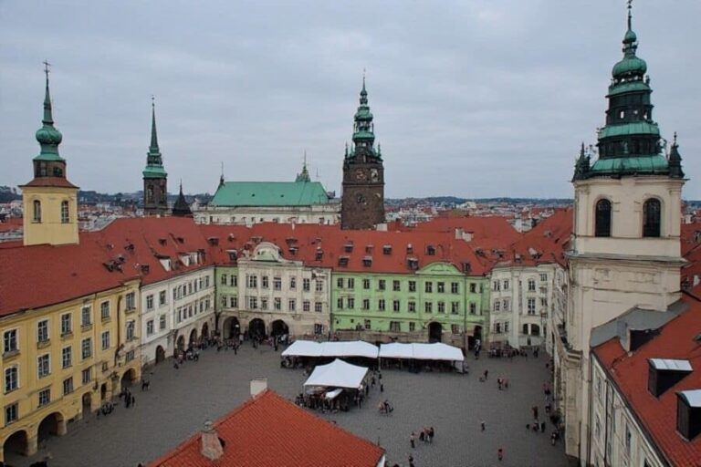 Aerial view of Prague's Old Town Square with pastel buildings, red-tiled roofs, and market stalls in the square.