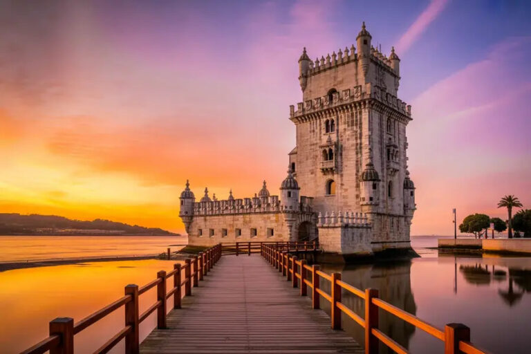 Belem Tower in Lisbon at sunset, a wooden walkway extends toward the stone fortress in calm water.