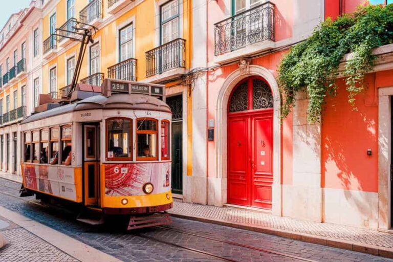 Historic yellow tram on a cobblestone street with pastel buildings and a bright red door nearby.