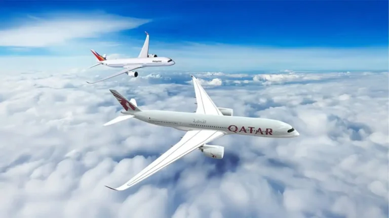 Qatar Airways plane in the foreground flying above fluffy clouds with another jet in the distance against a blue sky.