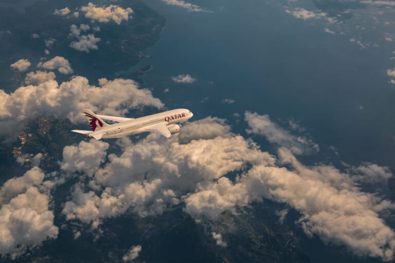 Qatar Airways passenger jet flying high above clouds over a blue ocean/landscape scene.