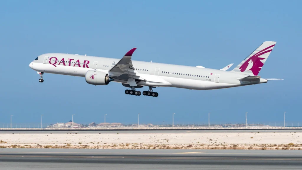 Qatar Airways wide-body jet lifting off from a runway with clear blue sky in the background.