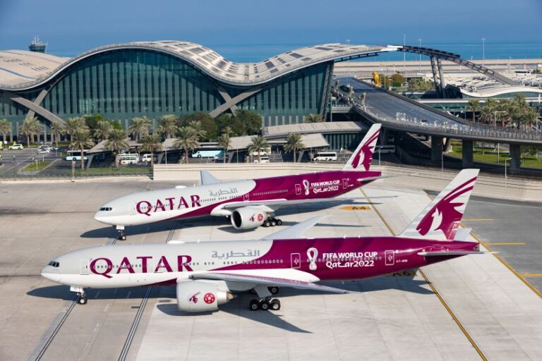 Two Qatar Airways jets parked on the tarmac beside a curved modern airport terminal, with FIFA World Cup Qatar 2022 branding on the fuselages.