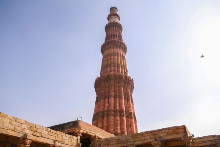 Tall red-brick minaret rises above a stone terrace against a clear blue sky, with a bird nearby.